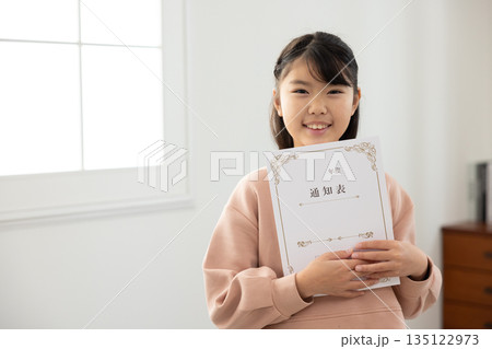通知表を持ち、不安そうな表情を見せる小学生の女の子 135122973