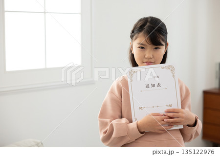 通知表を持ち、不安そうな表情を見せる小学生の女の子 135122976