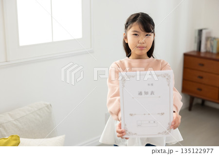 通知表を持ち、不安そうな表情を見せる小学生の女の子 135122977