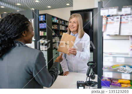 Female customer talking to a pharmacist at the cashier desk 135123203