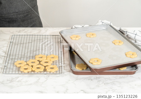 Partially filled cooling rack with cookies being moved from the baking tray. A step in the Easter Cookie Sandwich with Raspberry Buttercream preparation. Partially filled cooling rack with cookies being moved from the baking tray. A step in the Easter Cookie Sandwich with Raspberry Buttercream preparation. 135123226