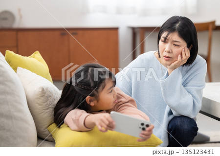 スマートフォンに夢中な娘を心配そうに見つめる母親 135123431