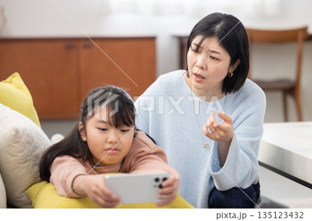 スマートフォンに夢中な娘を心配そうに見つめる母親 スマートフォンに夢中な娘を心配そうに見つめる母親 135123432