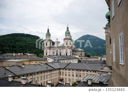 Panoramic view of Salzburg old town rooftops with cathedral towers and green alpine hills in background 135123683
