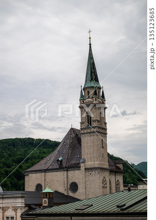 Historic church tower rising above Salzburg old town rooftops with green alpine hills in background 135123685