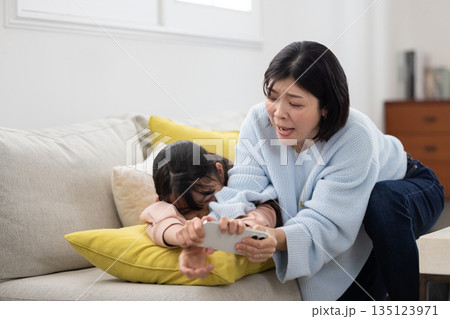 小学生の娘からスマートフォンを取り上げようとする母親 小学生の娘からスマートフォンを取り上げようとする母親 135123971