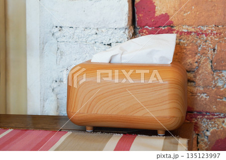 The tissues are in a rectangular wooden box, placed and colorful cloth on a wooden table, cement wall background The tissues are in a rectangular wooden box, placed and colorful cloth on a wooden table, cement wall background 135123997