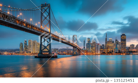 San Francisco city skyline with illuminated bridge and calm water at dusk creating peaceful urban atmosphere 135125451