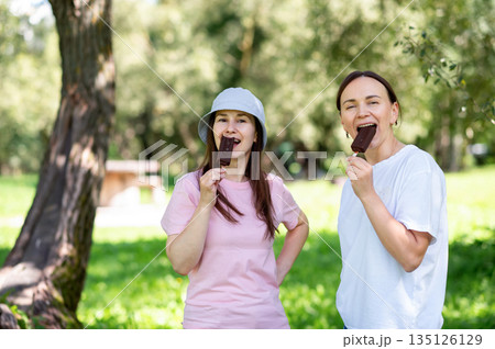 Chocolate ice cream on sticks eaten by two friends in summer park Chocolate ice cream on sticks eaten by two friends in summer park 135126129