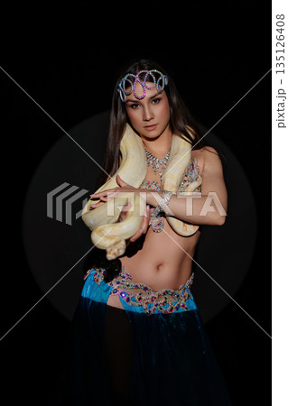 Woman performs dance with a snake in a dark setting during a cultural event in the evening 135126408