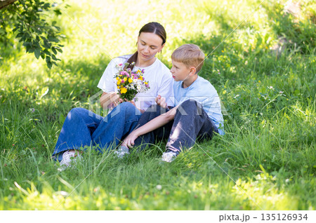 Mother and teen son enjoying time together with wildflowers in summer park Mother and teen son enjoying time together with wildflowers in summer park 135126934