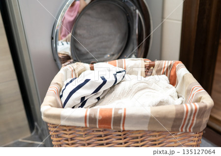 Wicker basket with dirty laundry in front of washing machine Wicker basket with dirty laundry in front of washing machine 135127064