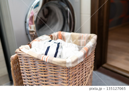 Wicker basket with dirty laundry in front of washing machine 135127065
