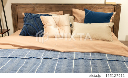 Cozy wooden bed with assorted pillows and blue blanket in bedroom 135127911