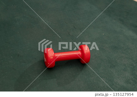 Single red dumbbell on dark green surface for fitness Single red dumbbell on dark green surface for fitness 135127954
