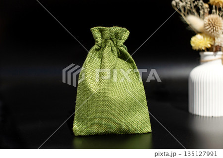Green burlap drawstring bag on black surface with dried flowers in vase 135127991
