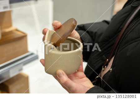 Female shopper examines ceramic container with wooden lid in store Female shopper examines ceramic container with wooden lid in store 135128001