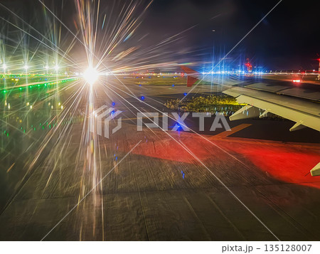 Night airport . An illuminated airport runway at night is captured from an airplane window with vivid starburst light trails and visible aircraft wing. Air travel, night aviation, runway lighting Night airport . An illuminated airport runway at night is captured from an airplane window with vivid starburst light trails and visible aircraft wing. Air travel, night aviation, runway lighting 135128007