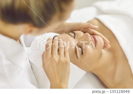 Close up photo of pretty young woman lying with closed eyes and having face or head massage in spa 135128049