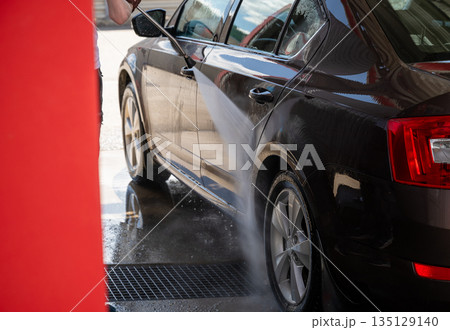 Man washing car with high pressure water at self service car wash station on sunny day 135129140