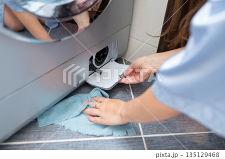 Woman cleaning washing machine drain filter through service hatch 135129468