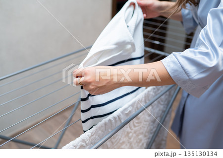 Woman's hands hanging freshly washed clothes on drying rack Woman's hands hanging freshly washed clothes on drying rack 135130134