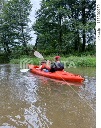 Father and son paddling a kayak on a calm river, view from behind Father and son paddling a kayak on a calm river, view from behind 135130979