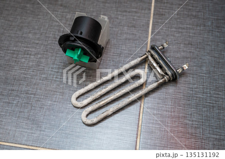Heating element and pump motor from a washing machine placed on tiled floor after removal Heating element and pump motor from a washing machine placed on tiled floor after removal 135131192