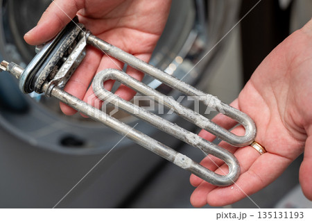 Hands holding washing machine heating element covered with limescale during appliance repair Hands holding washing machine heating element covered with limescale during appliance repair 135131193