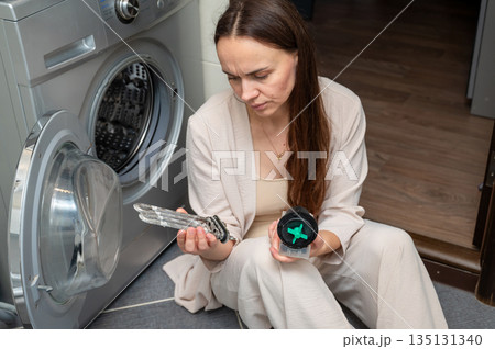 Woman examining washing machine parts  heating element and pump motor during home appliance repair 135131340