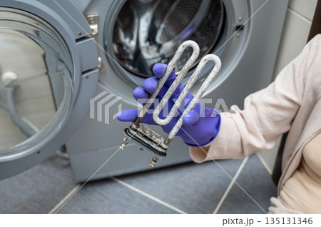 Person in gloves showing removed washing machine heating element covered with limescale 135131346