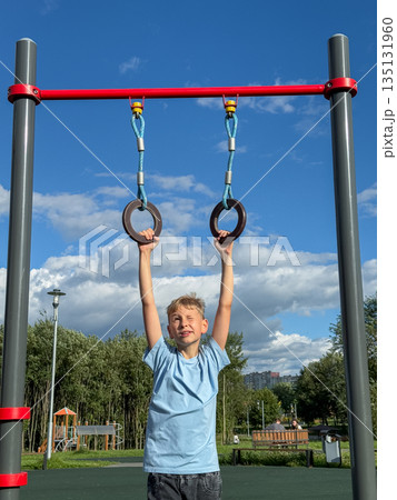 Teenage boy training on gymnastic rings at outdoor sports playground on a sunny summer day 135131960