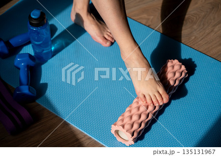 Female legs on foam roller doing myofascial massage with dumbbells and water bottle nearby Female legs on foam roller doing myofascial massage with dumbbells and water bottle nearby 135131967