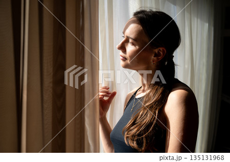 Thoughtful woman looking out the window in sunlight, cozy interior Thoughtful woman looking out the window in sunlight, cozy interior 135131968