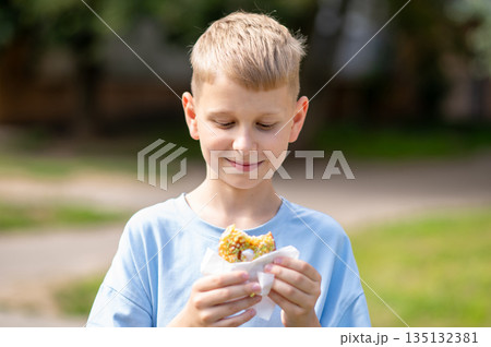 Happy teenage boy eating donut outdoors on a sunny day 135132381