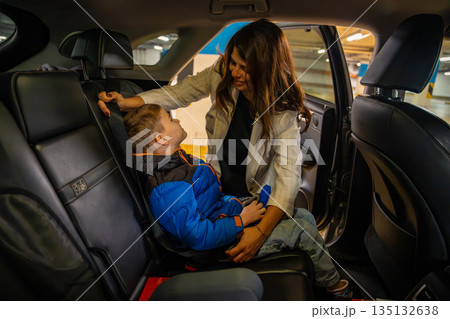 Mother fastening child into car seat inside vehicle interior before departure. Family safety routine, childcare responsibility and everyday transport moment during travel in real life environment Mother fastening child into car seat inside vehicle interior before departure. Family safety routine, childcare responsibility and everyday transport moment during travel in real life environment 135132638