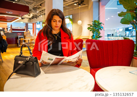 Woman reading menu while standing inside cafe in shopping mall. Everyday leisure choice, decision making process and lifestyle pause during urban routine in real life commercial environment 135132657