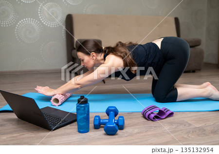 Woman exercising on yoga mat at home following online workout on laptop Woman exercising on yoga mat at home following online workout on laptop 135132954