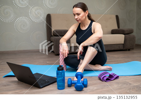 Woman exercising on yoga mat at home following online workout on laptop Woman exercising on yoga mat at home following online workout on laptop 135132955