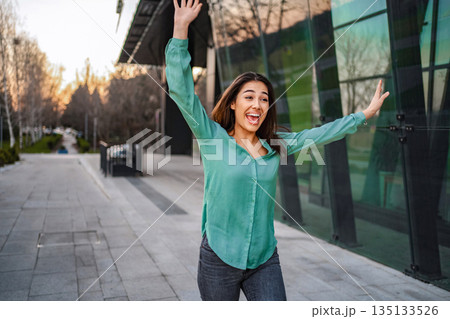 Young woman celebrating success in the city with arms raised Young woman celebrating success in the city with arms raised 135133526