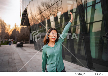 Excited businesswoman waving and laughing near an office building Excited businesswoman waving and laughing near an office building 135133529