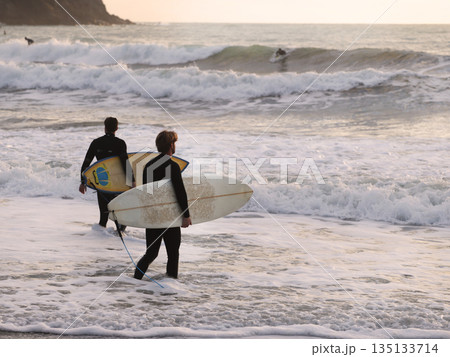 Surfer in warm wetsuit enters water with board at sunset. Winter sports in Italy. Health, sea, and nature. Surfer in warm wetsuit enters water with board at sunset. Winter sports in Italy. Health, sea, and nature. 135133714