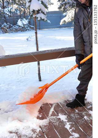 Removing a lot of snow by orange plastic shovel from wooden terrace 135133762