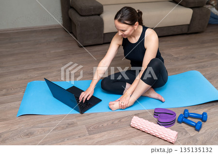 Young woman doing home workout with dumbbells, yoga mat, foam roller and resistance band 135135132