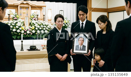 葬儀場で遺影を持つ息子と悲しみに暮れる喪主の三世代家族 135135649