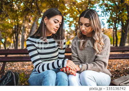 Two women sit on a bench holding hands in a sign of comfort and support Two women sit on a bench holding hands in a sign of comfort and support 135136742