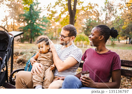 Mixed race couple is sitting on a park bench with their son Mixed race couple is sitting on a park bench with their son 135136797