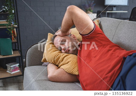 Man alone at home lying on sofa looking sad and distraught 135136922