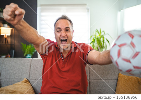 Excited middle aged man watching soccer game at home Excited middle aged man watching soccer game at home 135136956