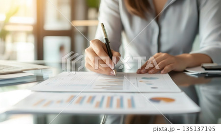 Businesswoman examining financial charts and graphs, taking notes during an office meeting, demonstrating professionalism and expertise in financial analysis 135137195